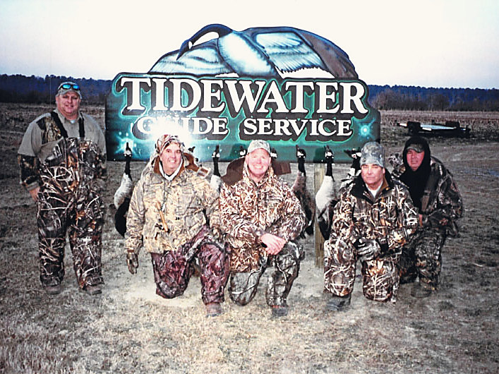 Five hunters kneeling at the Tidewater Guide Service sign with their geese